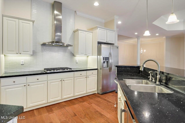 kitchen featuring wall chimney exhaust hood, decorative light fixtures, white cabinetry, stainless steel appliances, and sink