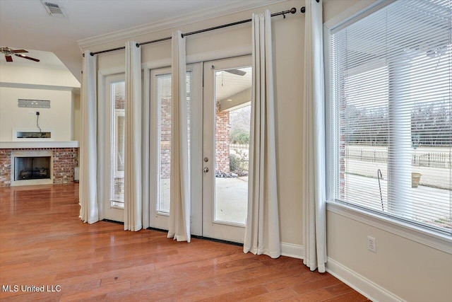 doorway featuring ceiling fan, light wood-type flooring, ornamental molding, and a fireplace