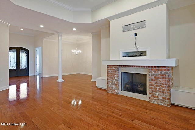 unfurnished living room featuring crown molding, decorative columns, a brick fireplace, and french doors