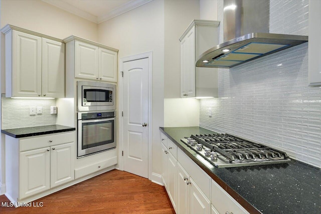 kitchen featuring appliances with stainless steel finishes, extractor fan, white cabinets, ornamental molding, and backsplash