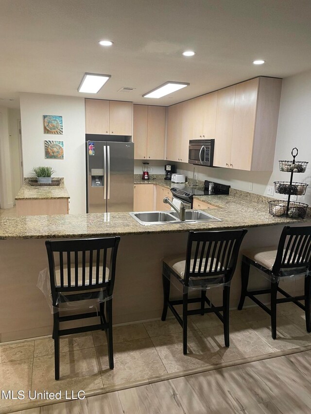 kitchen with appliances with stainless steel finishes, kitchen peninsula, and light wood-type flooring