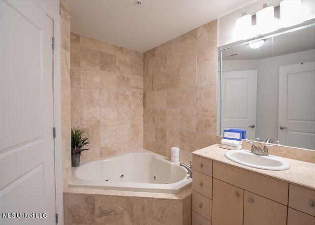 bathroom featuring vanity, a relaxing tiled tub, and tile walls