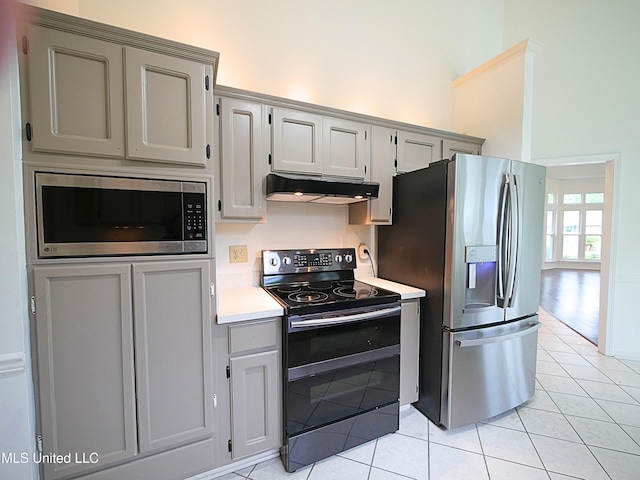 7869 Hilo Way, Diamondhead, MS 39525 - kitchen featuring stainless steel appliances, under cabinet range hood, light tile patterned floors, gray cabinets, and a high ceiling