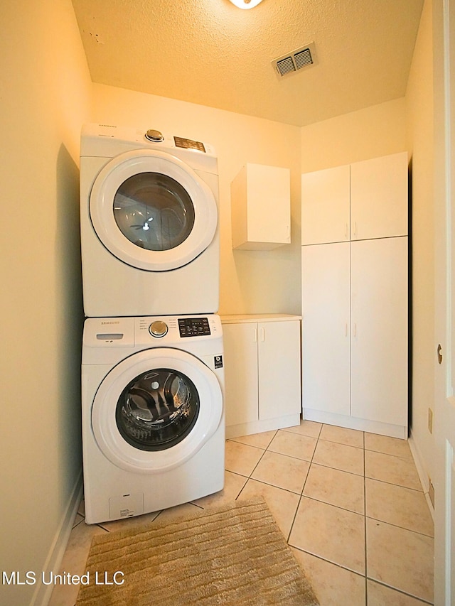 7869 Hilo Way, Diamondhead, MS 39525 - laundry room featuring stacked washer / drying machine, cabinet space, light tile patterned floors, baseboards, and a textured ceiling