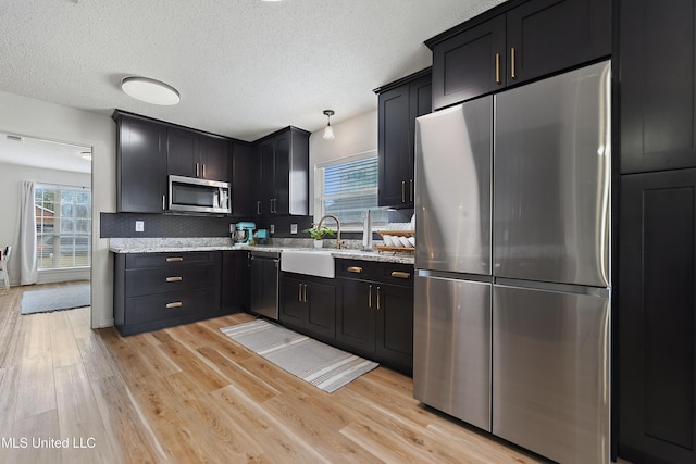 kitchen featuring appliances with stainless steel finishes, light hardwood / wood-style floors, light stone counters, and tasteful backsplash