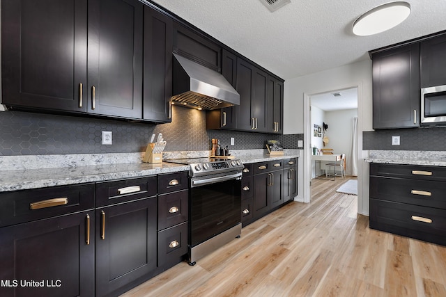 kitchen with light stone countertops, stainless steel appliances, light hardwood / wood-style flooring, and wall chimney range hood