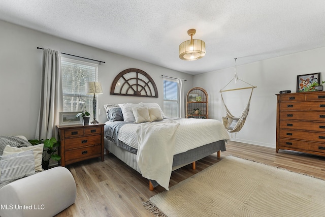 bedroom featuring multiple windows, light hardwood / wood-style floors, and a textured ceiling