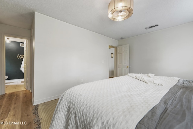 bedroom with connected bathroom, hardwood / wood-style floors, and a textured ceiling