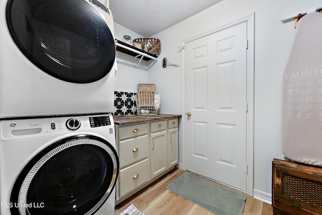 washroom featuring a textured ceiling, cabinets, light wood-type flooring, and stacked washer / dryer