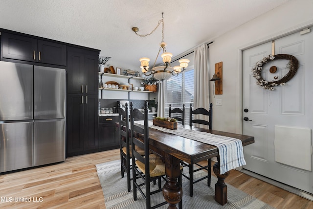 dining space with light wood-type flooring, a textured ceiling, and a chandelier