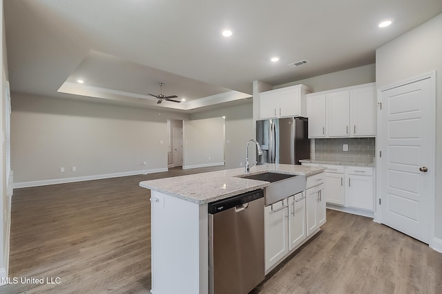 kitchen with stainless steel appliances, white cabinets, an island with sink, and a tray ceiling