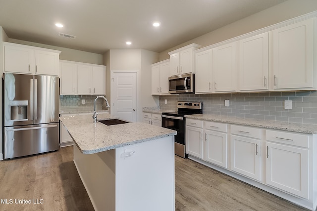 kitchen featuring a center island with sink, white cabinetry, appliances with stainless steel finishes, sink, and light hardwood / wood-style flooring