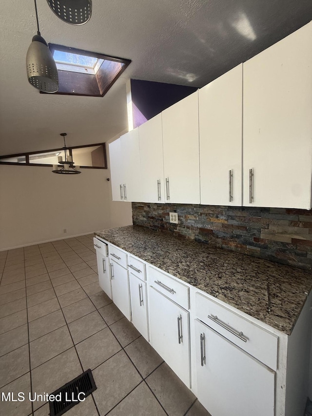 kitchen featuring decorative light fixtures, decorative backsplash, white cabinetry, a skylight, and light tile patterned floors