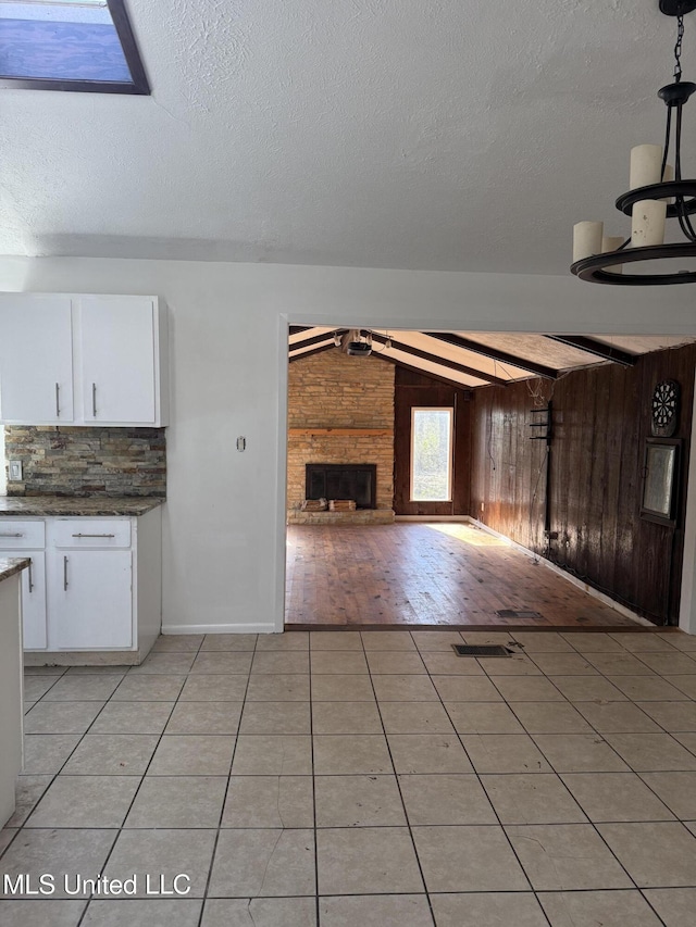 unfurnished living room featuring vaulted ceiling, a brick fireplace, wooden walls, a textured ceiling, and light tile patterned floors