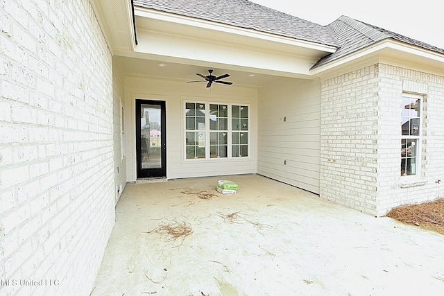 entrance to property featuring a shingled roof, brick siding, a patio, and a ceiling fan