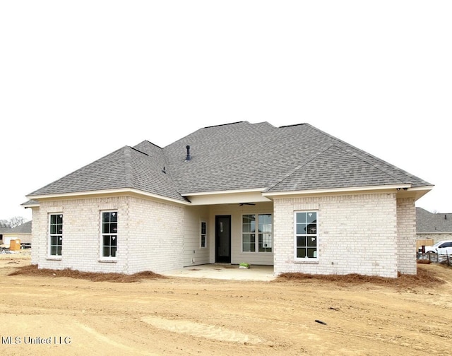 rear view of house with roof with shingles, brick siding, and a patio