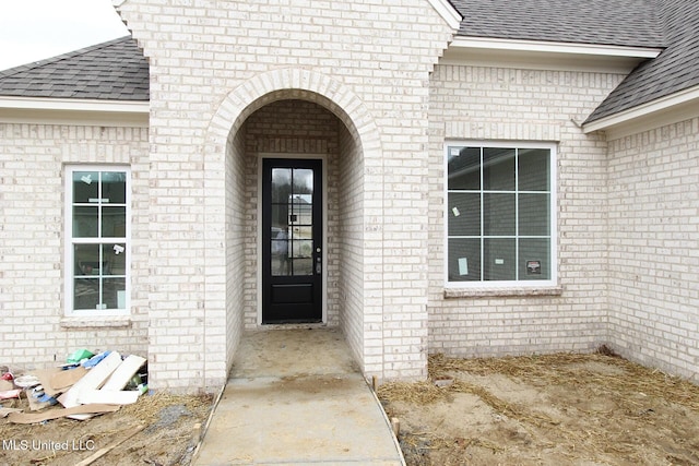 doorway to property with a shingled roof and brick siding