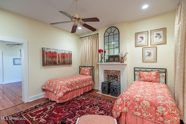 bedroom featuring a ceiling fan, a fireplace, wood finished floors, baseboards, and recessed lighting
