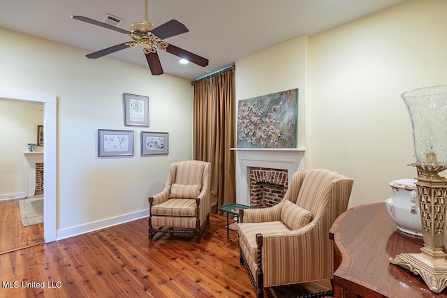 living area with visible vents, hardwood / wood-style floors, a fireplace, baseboards, and a ceiling fan