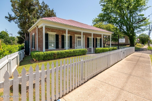 view of property exterior with a porch, brick siding, a fenced front yard, and metal roof