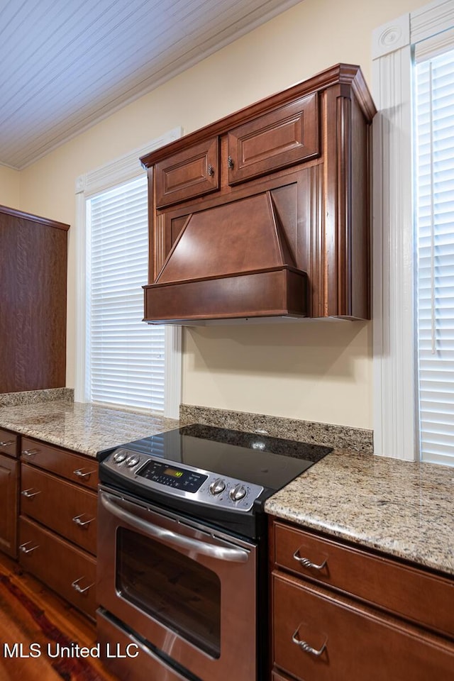 kitchen with crown molding, light stone countertops, dark brown cabinetry, stainless steel range with electric stovetop, and custom exhaust hood