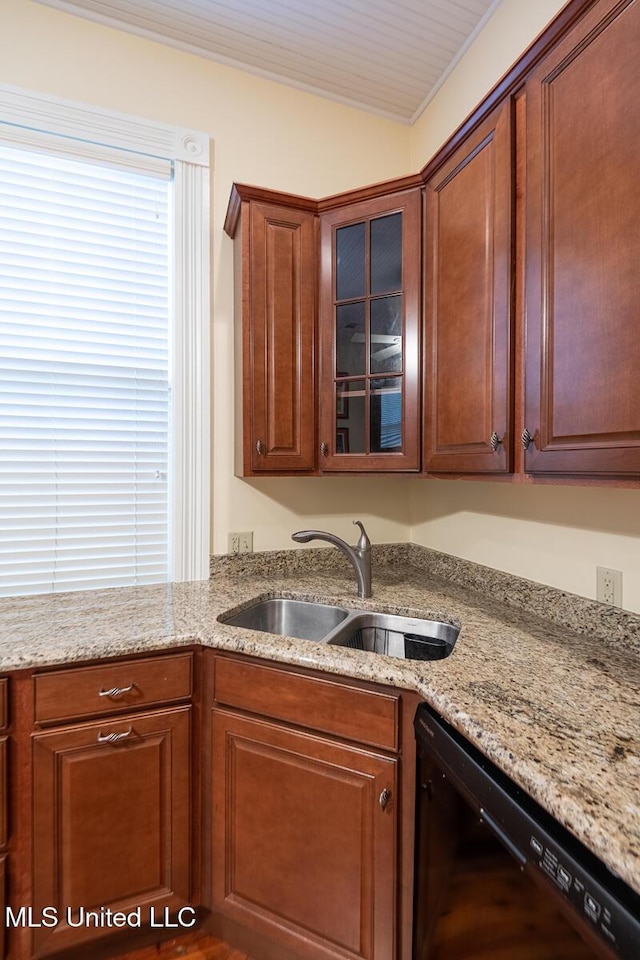 kitchen with brown cabinets, light stone countertops, a sink, black dishwasher, and glass insert cabinets