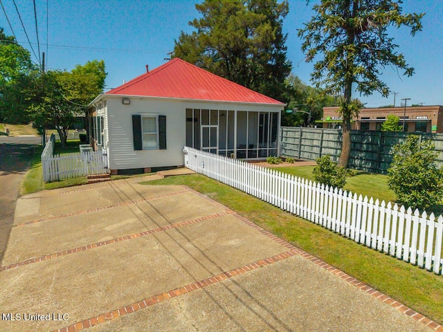 back of house featuring metal roof, a fenced backyard, a sunroom, and a patio area