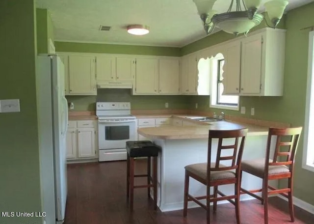 kitchen with white cabinetry, a kitchen bar, white appliances, and kitchen peninsula