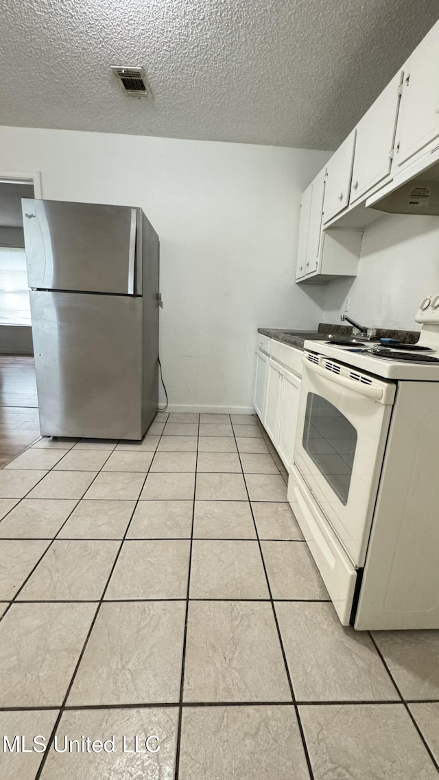 kitchen featuring electric stove, stainless steel fridge, white cabinetry, a textured ceiling, and light tile patterned flooring