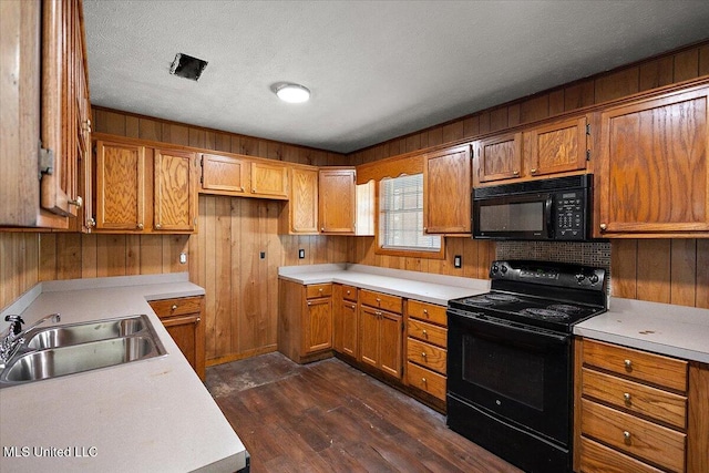 kitchen featuring dark wood-type flooring, black appliances, sink, wooden walls, and a textured ceiling