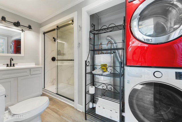 bathroom with hardwood / wood-style floors, vanity, crown molding, a shower with shower door, and stacked washer / dryer