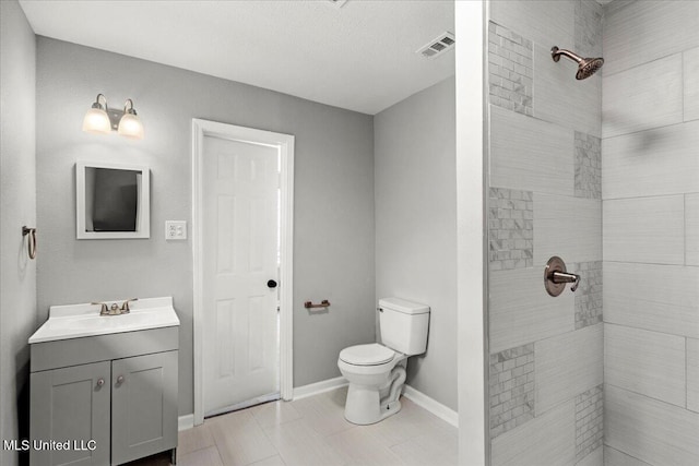 bathroom with a tile shower, vanity, and toilet