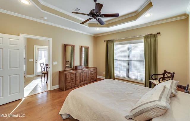 bedroom with light wood finished floors, baseboards, visible vents, a tray ceiling, and crown molding