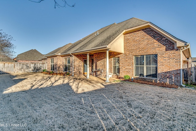 back of house with a patio, brick siding, a shingled roof, and fence