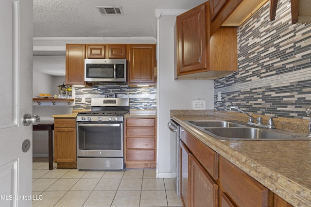 kitchen featuring sink, light tile patterned floors, stainless steel appliances, crown molding, and a textured ceiling