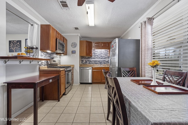 kitchen with light tile patterned floors, crown molding, ceiling fan, stainless steel appliances, and decorative backsplash