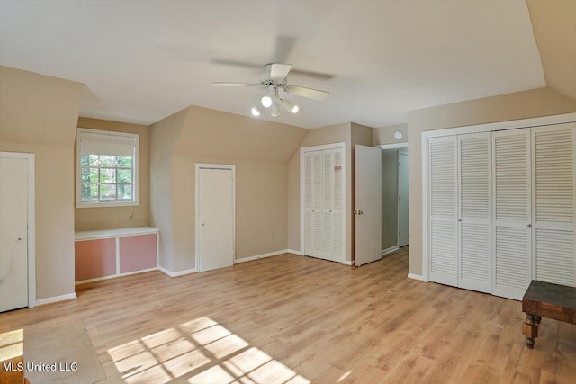 unfurnished bedroom with ceiling fan, multiple closets, lofted ceiling, and light wood-type flooring