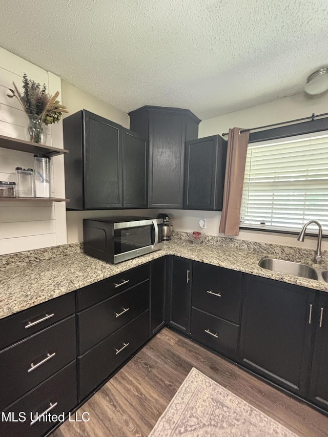 kitchen with dark wood finished floors, dark cabinetry, a sink, stainless steel microwave, and a textured ceiling