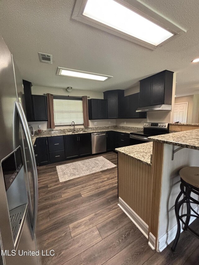 kitchen with dark cabinets, visible vents, a peninsula, a textured ceiling, and appliances with stainless steel finishes
