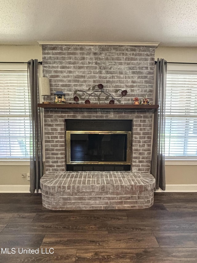 details featuring a textured ceiling, wood finished floors, a brick fireplace, and baseboards