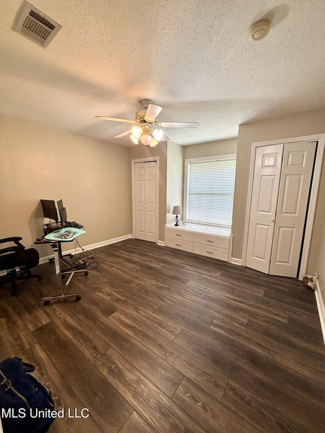 interior space featuring visible vents, dark wood-style flooring, baseboards, a textured ceiling, and ceiling fan