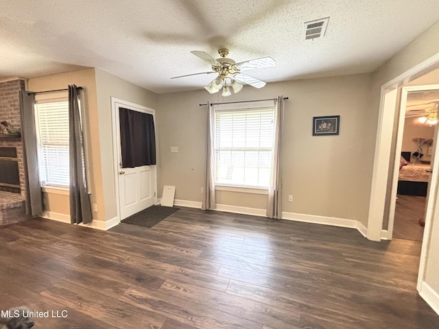 unfurnished living room featuring dark wood-style floors, visible vents, baseboards, a textured ceiling, and ceiling fan