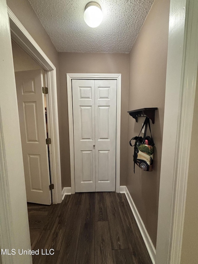 hallway featuring baseboards, dark wood-style flooring, and a textured ceiling