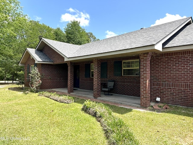 back of property featuring brick siding, a yard, and roof with shingles