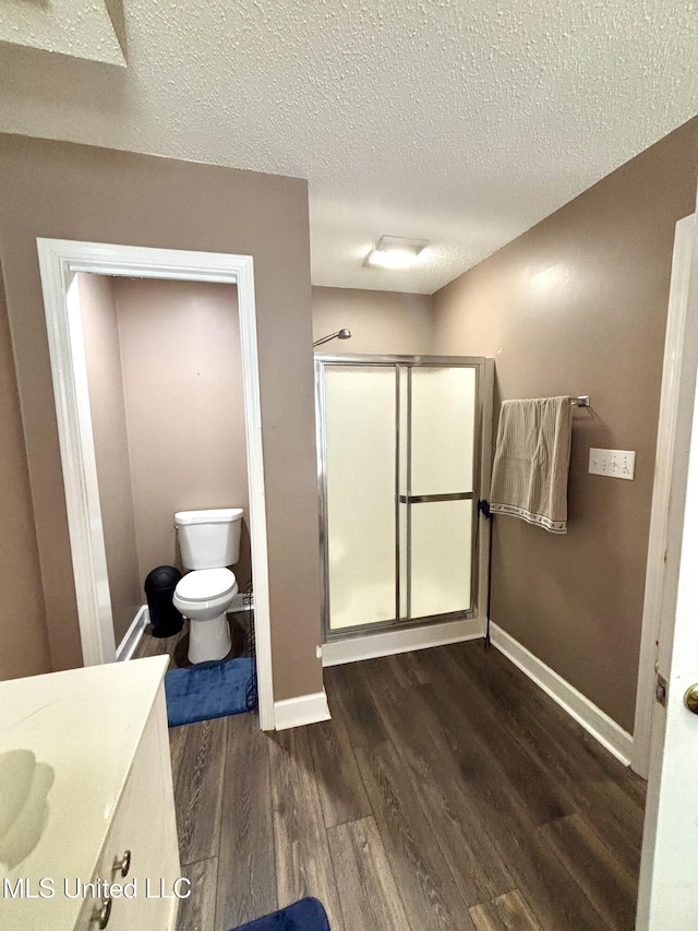 full bath featuring a shower stall, wood finished floors, toilet, vanity, and baseboards