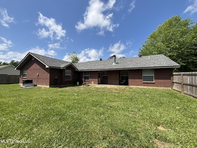 back of property featuring brick siding, fence, and a yard