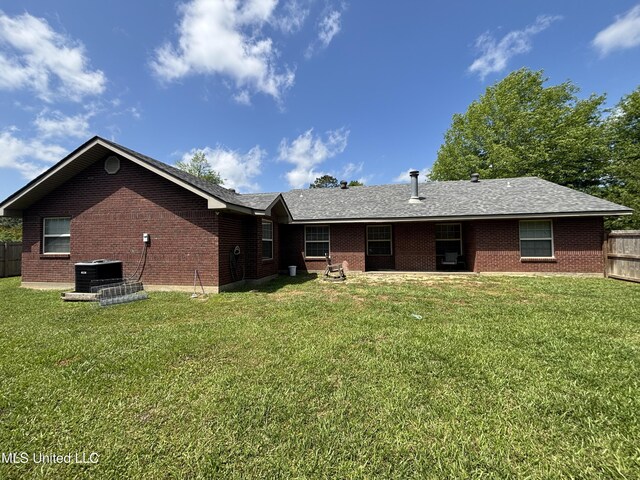 back of property featuring brick siding, fence, and a yard