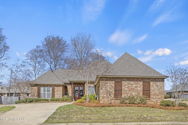 view of front of home with a front yard, fence, brick siding, and roof with shingles