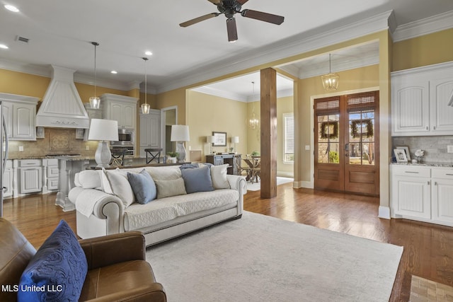 living room featuring baseboards, recessed lighting, ornamental molding, dark wood-type flooring, and ceiling fan with notable chandelier