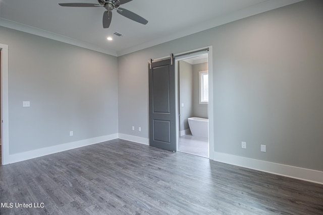 unfurnished bedroom with ensuite bathroom, a barn door, ceiling fan, dark wood-type flooring, and crown molding